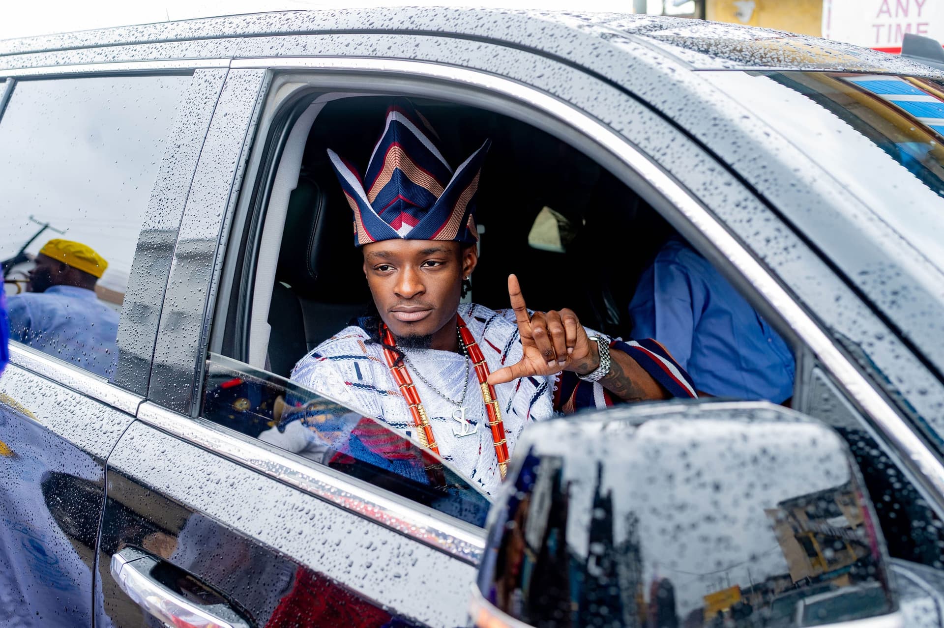 Mr. Strangeloots in a beaded crown, arriving through the rain in Lagos